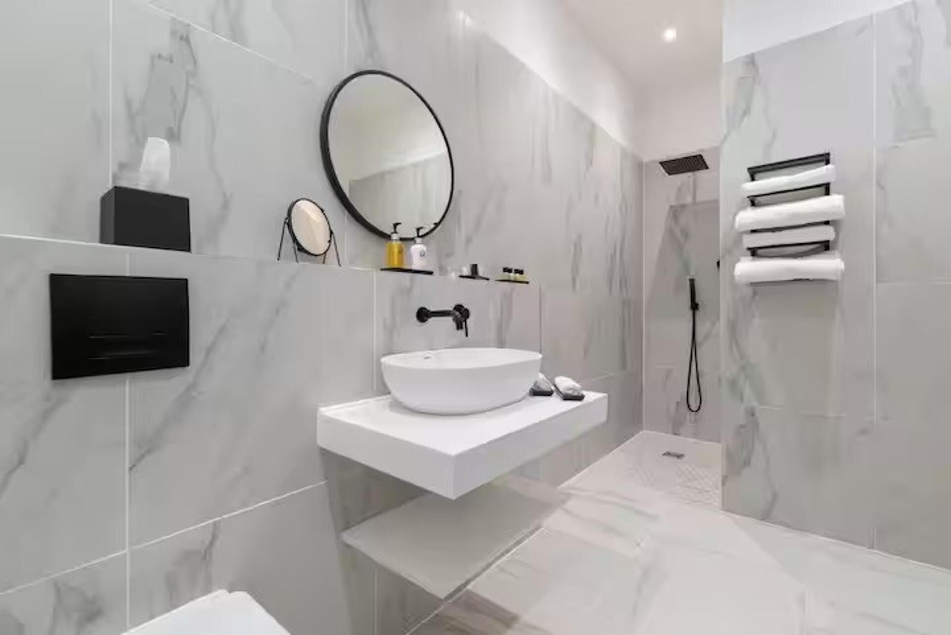A modern bathroom with a white sink, a round mirror, and a towel rack.