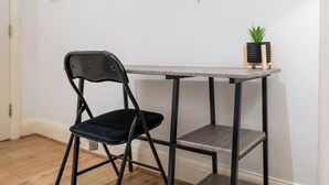 Ein kleines Zimmer mit klappbarem Stuhl, einem kleinen Tisch und einer Topfpflanze.