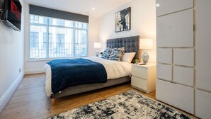 Ein modernes Schlafzimmer mit einem großen Bett, Nachttischen, einem Fernseher und einem Fenster mit Blick auf die Stadt.