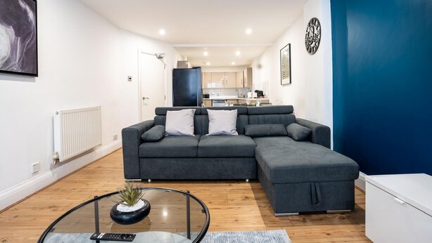 Ein modernes Wohnzimmer mit einem Ecksofa, einem Glastisch und einer Küche im Hintergrund.