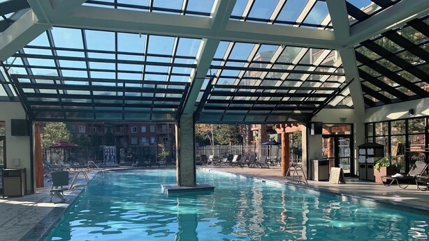 Une piscine intérieure à l’eau d’un bleu cristallin, entourée de chaises longues et d’un espace abrité doté d’un plafond en verre.