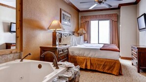 Une chambre d’hôtel avec une grande baignoire, un lit avec une base marron, un ventilateur de plafond et une fenêtre avec des rideaux.