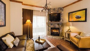 Un salon chaleureux avec une cheminée en pierre, des canapés en cuir, un téléviseur à écran plat et un tableau accroché au mur.