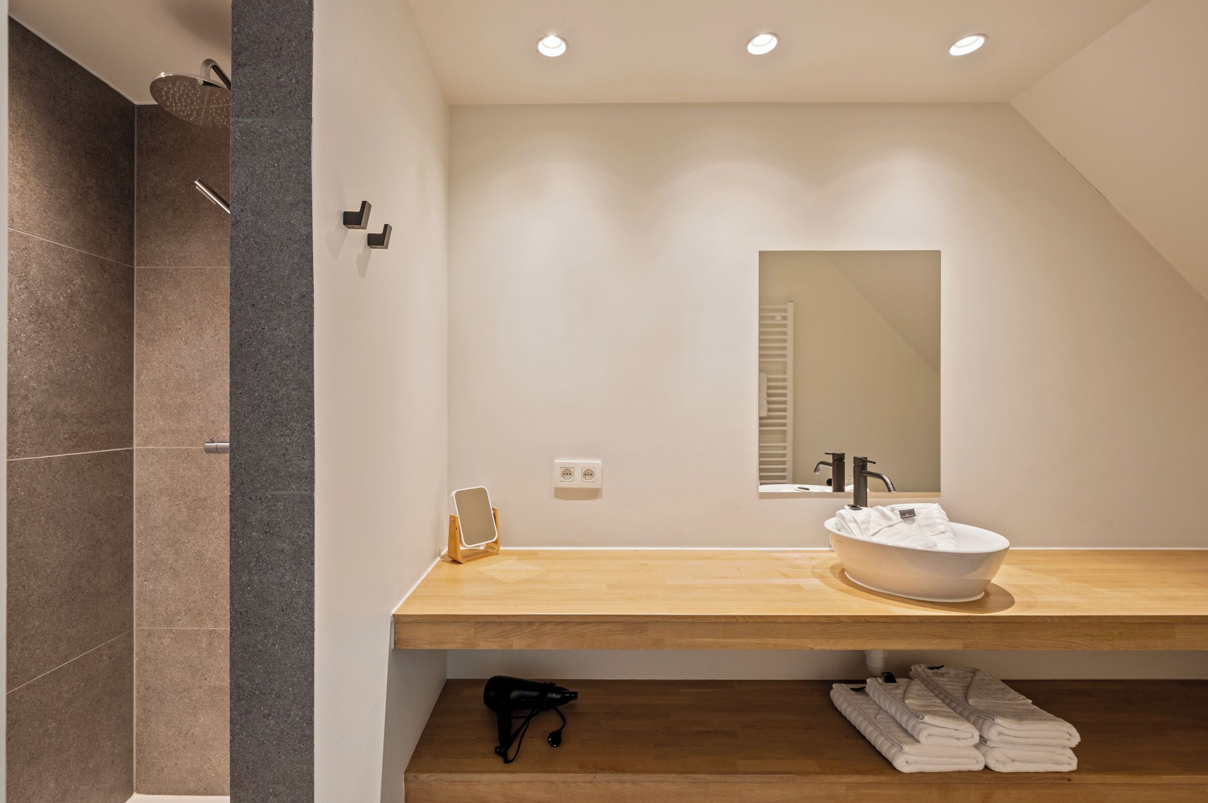 Een moderne badkamer met een houten wastafel, een grote spiegel en een inloopdouche.