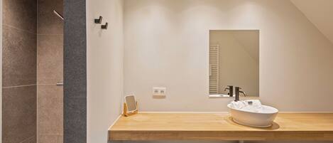 Een moderne badkamer met een houten wastafel, een grote spiegel en een inloopdouche.