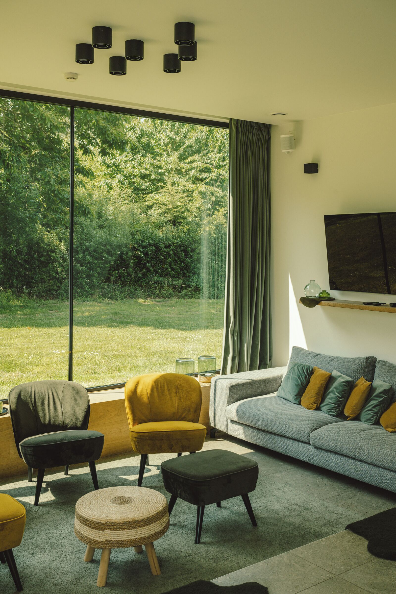 A modern living room with a large window, a grey sofa, yellow armchairs, and a round ottoman.