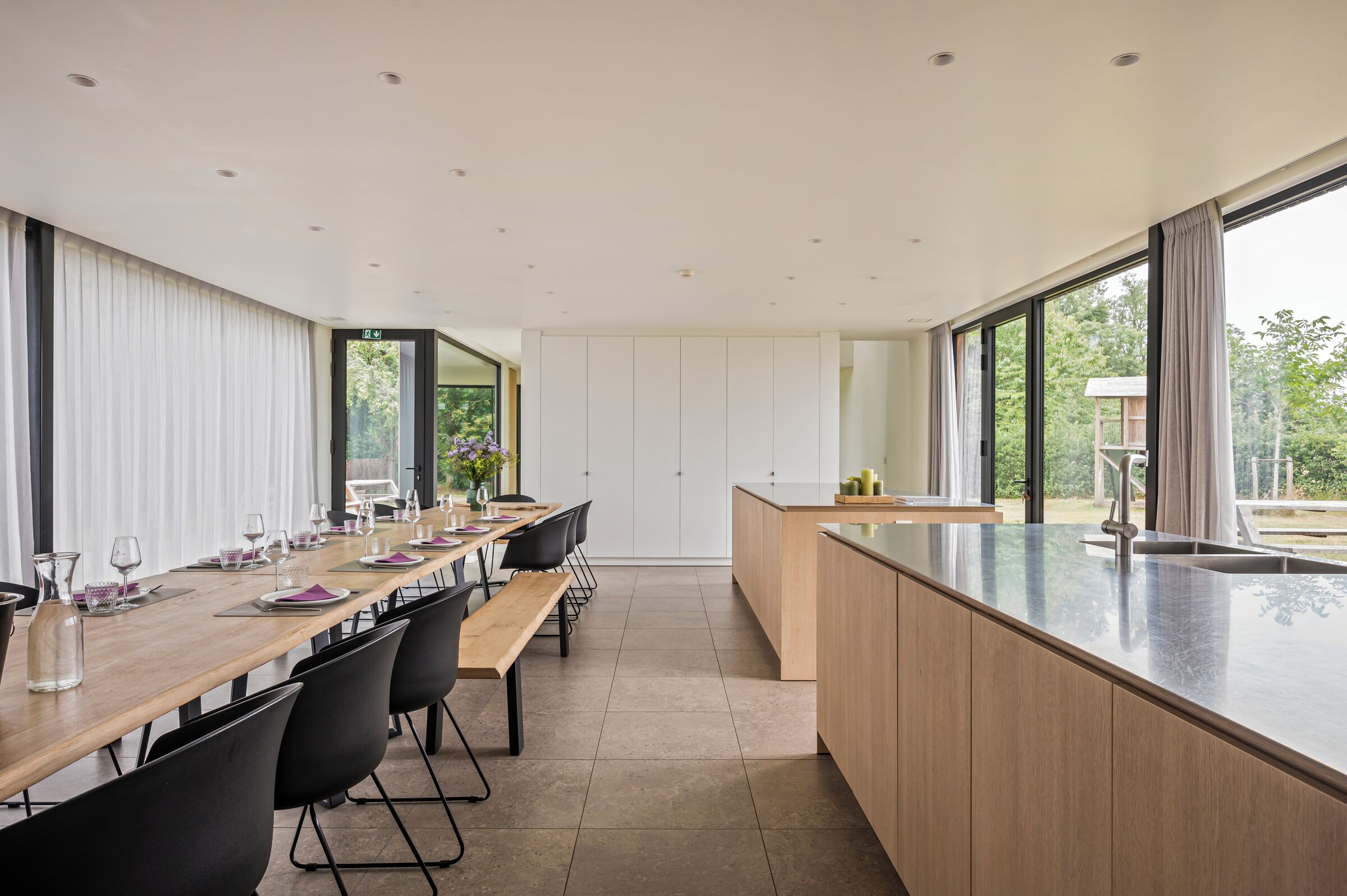 Une cuisine moderne avec une longue table à manger, des chaises noires et une grande fenêtre.