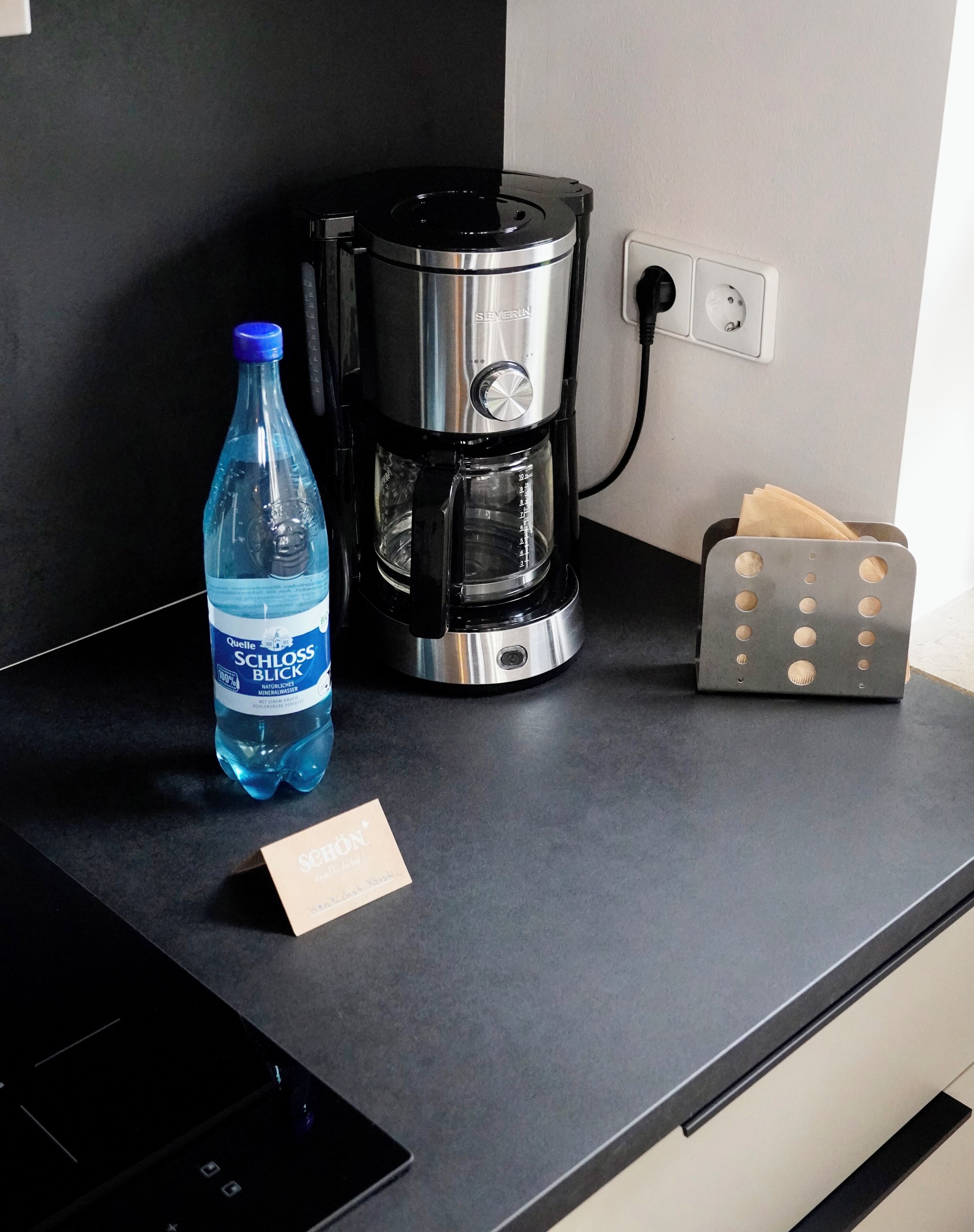 Un comptoir de cuisine avec une machine à café, une bouteille d’eau et une boîte de mouchoirs.