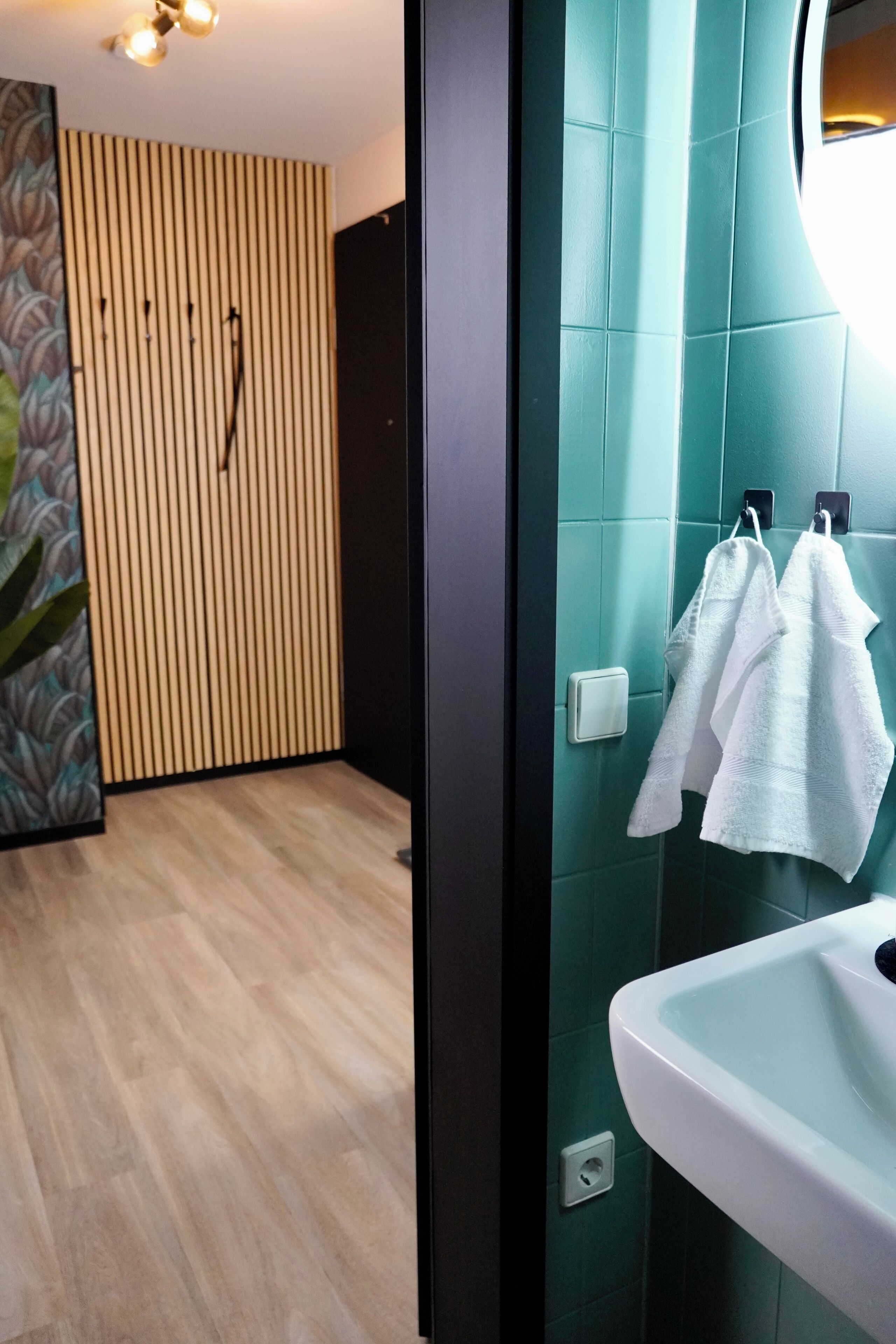Une salle de bain moderne avec un mur recouvert de carreaux verts, un lavabo blanc et deux serviettes blanches suspendues à un porte-serviettes.