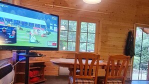 A wooden interior with a television displaying a sports event, a dining table, and chairs. - Chalet in the forest - HOUSE WITH LIFE AND LOVE FOR PEOPLE AND DOGS (Borkwalde)