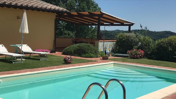 Ein Swimmingpool mit einer Pergola, Liegestühlen und Topfpflanzen.