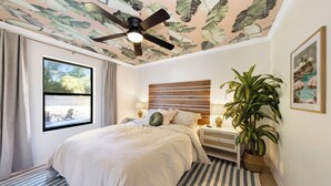 A bedroom with a large bed, a ceiling fan, a window with curtains, a bedside table with a lamp, and a potted plant. - Relax and Play - Heated Pool + Game Shed + Minutes to the Beach (St. Augustine)
