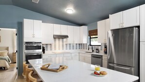 A modern kitchen with white cabinets, stainless steel appliances, and a marble island. - Relax and Play - Heated Pool + Game Shed + Minutes to the Beach (St. Augustine)
