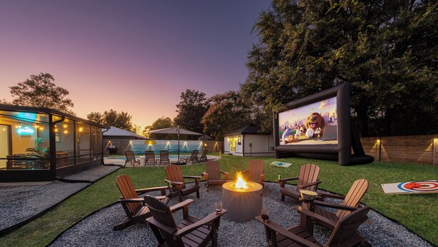 An outdoor patio area with Adirondack chairs, a fire pit, and a large screen for outdoor movies. - Relax and Play - Heated Pool + Game Shed + Minutes to the Beach (St. Augustine)