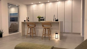 A modern kitchen with two wooden bar stools, a small island, and a built-in oven. - Quinta do Vale- Oasis Vila  (Sesimbra)