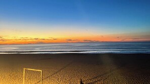 A beach with a goalpost in the foreground and a sunset in the background.
