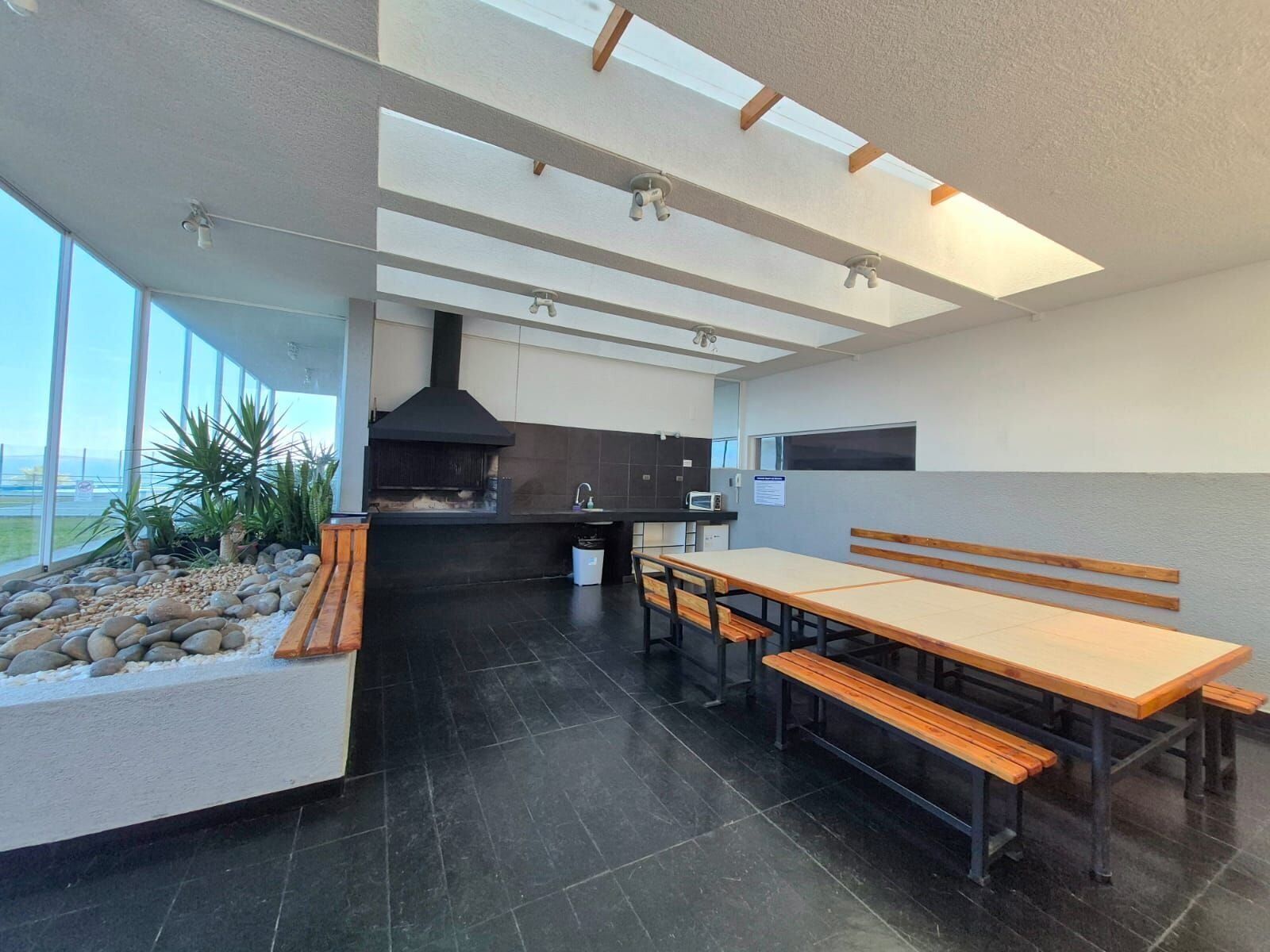 Una cocina moderna con horno integrado, un comedor con bancos y vistas a través de amplios ventanales.