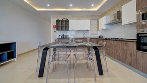 A modern kitchen with a central island, clear chairs, and built-in appliances. - Swieqi, Luxury Apartmen/3BD- 2BH,sleeps 6 (Is-Swieqi)