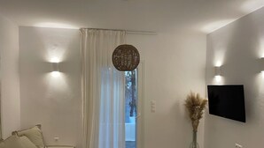 Un saló modern amb un sofà, un televisor de pantalla plana, una finestra gran amb cortines transparents i un llum decorativa teixida.