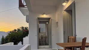Un balcó amb una taula i cadires de fusta, una porta que dona a una habitació interior, i una vista del cel.