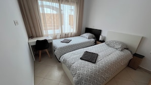 Una camera d'albergo con due letti, una scrivania e una sedia.
