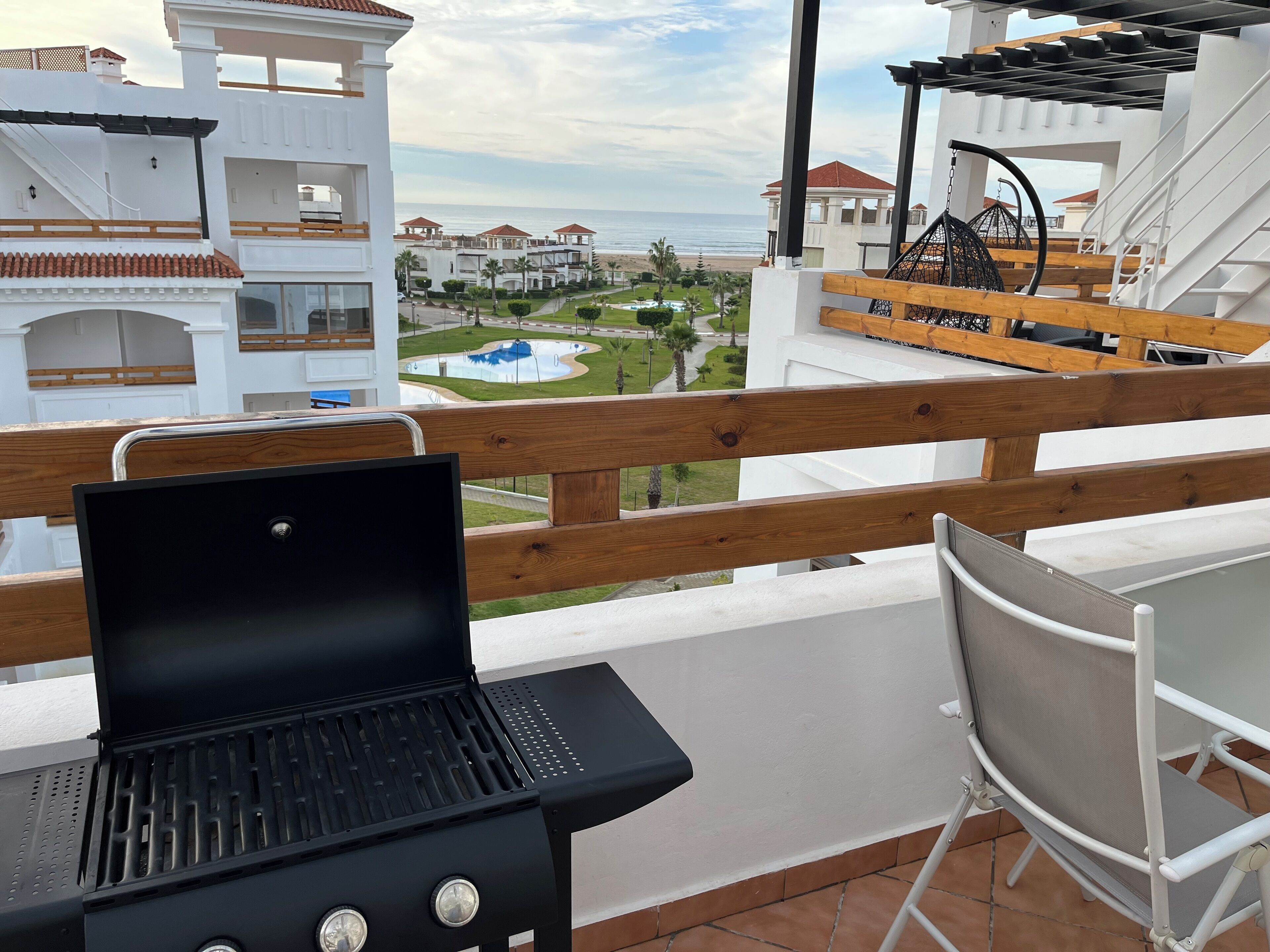 Un balcon avec un barbecue, une chaise et une vue sur une piscine et des immeubles.