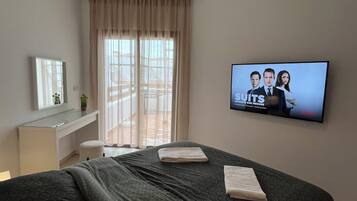 Hotelkamer met een bed, een tv waarop een film draait, een raam met gordijnen en een klein bureau met een plant.