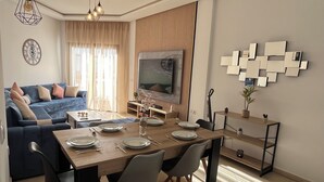 Un soggiorno moderno con un divano, un tavolo da pranzo per quattro persone, una televisione e un elemento decorativo a parete.