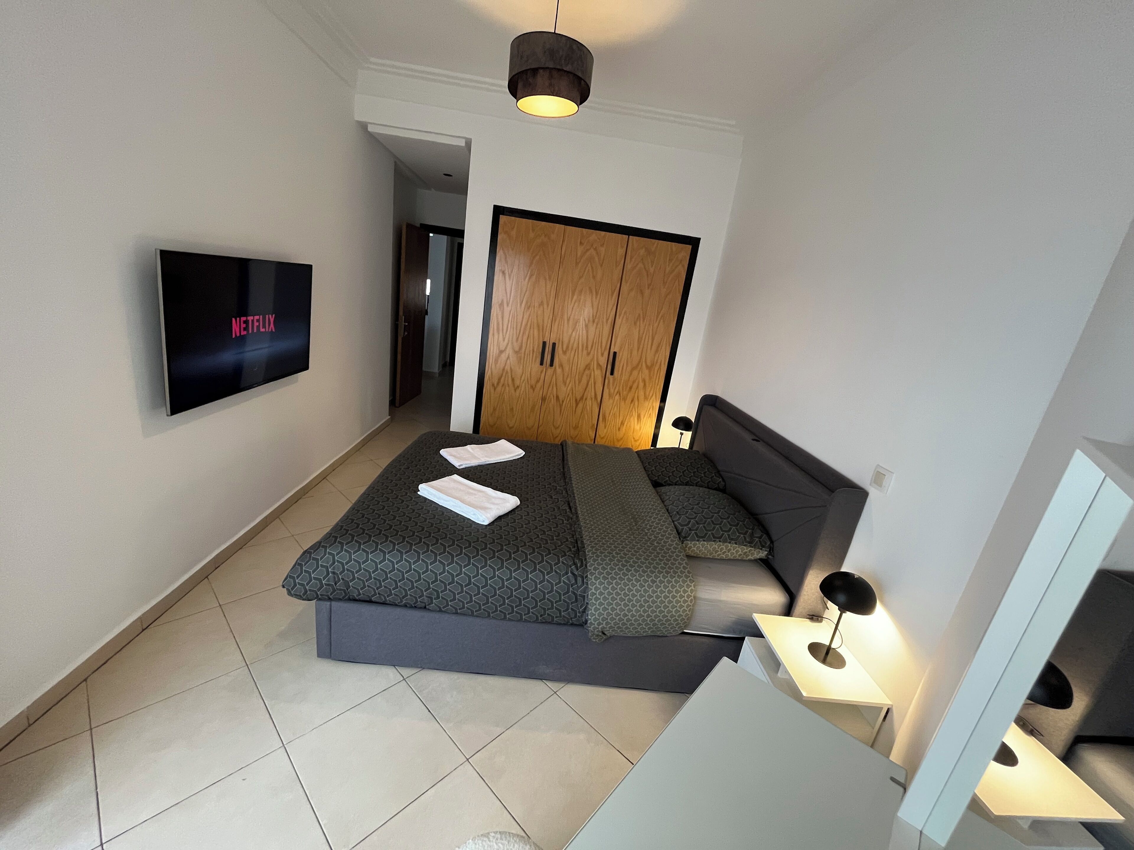 Ein modernes Schlafzimmer mit Bett, Fernseher, Kleiderschrank und Nachttisch.