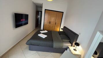 Ein modernes Schlafzimmer mit Bett, Fernseher, Kleiderschrank und Nachttisch.