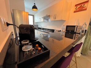 A modern kitchen with a large island, a built-in grill, and a microwave. - Beachfront Apartment, Private Solarium, 4 Pools, Secure Residence, WiFi, Parking (Asilah)