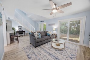 Ein geräumiges Wohnzimmer mit grauem Sofa, Couchtisch und Deckenventilator.