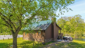 A cabin with a stone foundation, a porch with a table and chairs, and a view of a lake. - Riverfront Little Red Trout Cabin, Hot Tub & Views (Heber Springs)