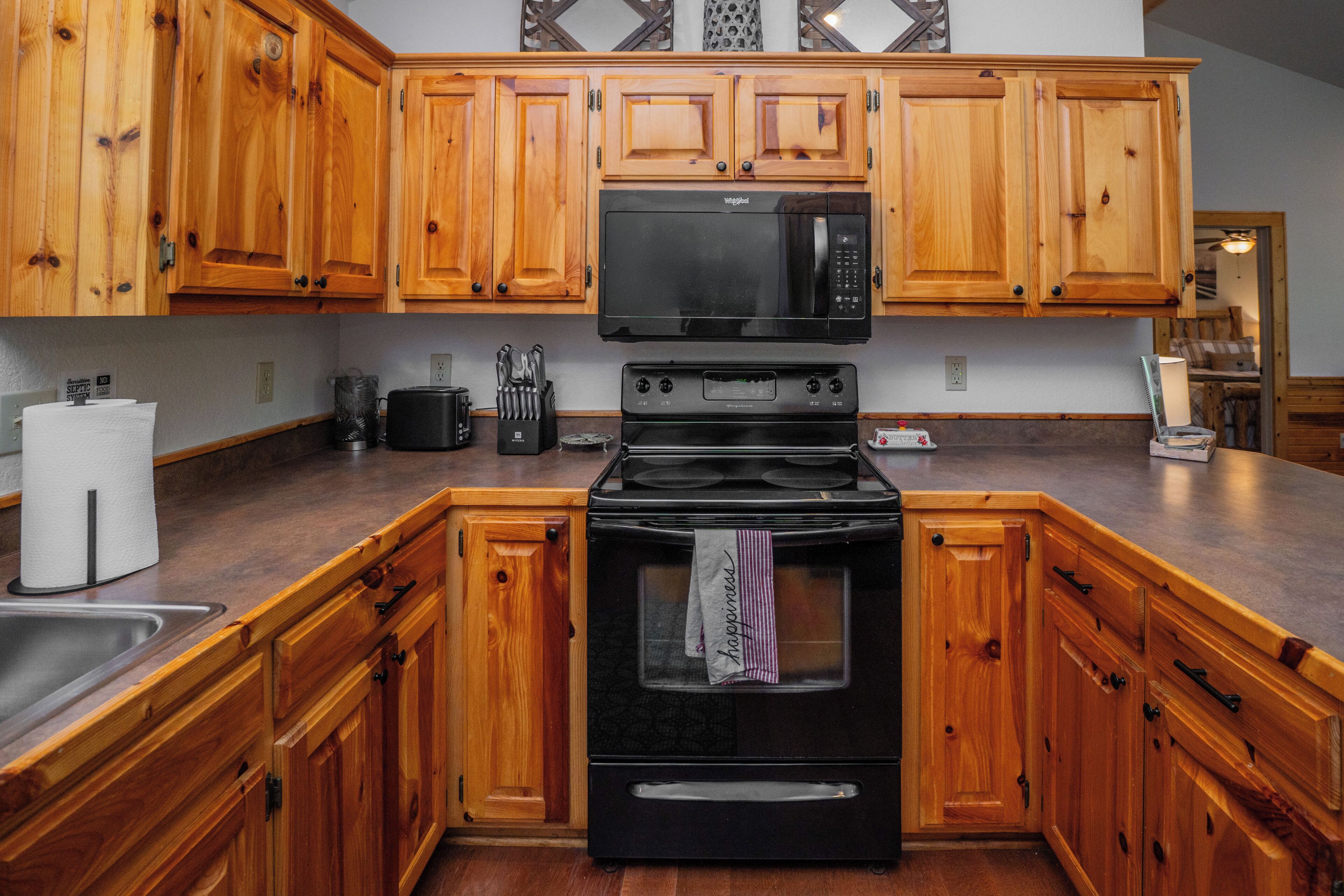A kitchen with wooden cabinets, a black microwave, a stove, and a sink.