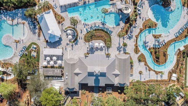 Eine Vogelperspektive zeigt ein Resort mit mehreren Schwimmbecken, einem großen Hauptgebäude und umliegenden, angelegten Grünflächen.