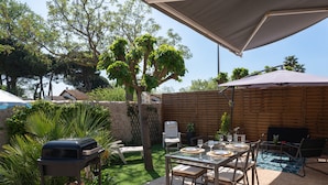 A patio area with a dining table set for four, surrounded by chairs, a barbecue grill, and a covered seating area with an umbrella. - Charmante maison climatisée à 500m de la plage (Vias)
