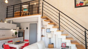 A modern kitchen with a dining area, a staircase with wooden steps, and a white sofa. - Charmante maison climatisée à 500m de la plage (Vias)