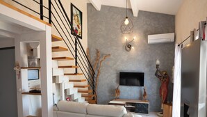 A modern living room with a staircase, a flat-screen TV, and a fireplace. - Charmante maison climatisée à 500m de la plage (Vias)