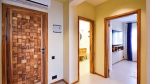 A hallway with a wooden door, a white wall with a thermostat, and a glimpse of a bathroom with a blue curtain. - Castle Residence by Aura  (Jambiani)