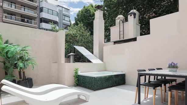 A modern outdoor patio with a white lounge chair, a hot tub, and a dining area with chairs and a table.