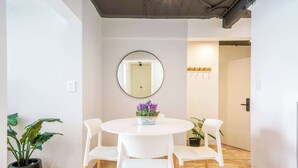 A dining area with a round table, four white chairs, a potted plant with purple flowers, and a round mirror on the wall.