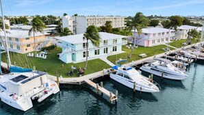 Una marina con varios barcos amarrados, un edificio azul claro con balcón y un edificio rosa con escalera.