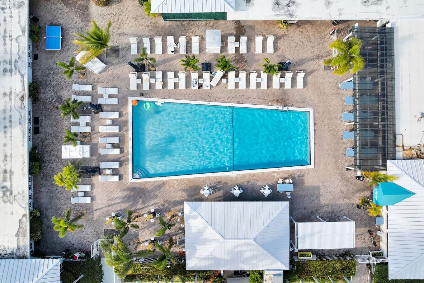 An aerial view of a resort with a large rectangular pool, multiple lounge chairs, and palm trees.