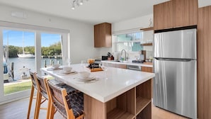 A modern kitchen with a large island, stainless steel appliances, and a view of a marina. - Waterfront Retreat with Marina Views & Pool (Marathon)