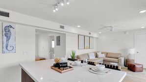 A modern living room with a large white marble island, a beige sofa, and a ceiling fan. - Waterfront Retreat with Marina Views & Pool (Marathon)