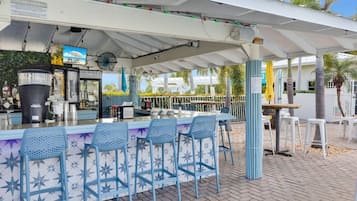 Un espace bar extérieur doté d’un auvent blanc, de chaises bleues et d’un comptoir avec un distributeur de boissons.