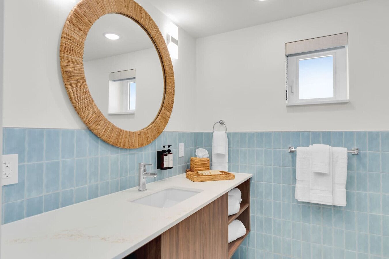 A bathroom with a round mirror, a sink, a window, and a towel rack.