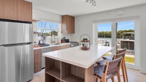 A modern kitchen with a large island, stainless steel appliances, wooden cabinets, and a view of a boat dock through a sliding glass door. - Waterfront Escape with Pool, Tiki, Breakfast & Marina (Marathon)