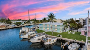 A marina with boats docked, a building with a light blue facade, and a sunset sky. - Waterfront Escape with Pool, Tiki, Breakfast & Marina (Marathon)