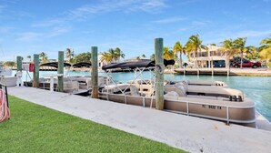 Marina com barcos atracados, área gramada e um edifício ao fundo com palmeiras.